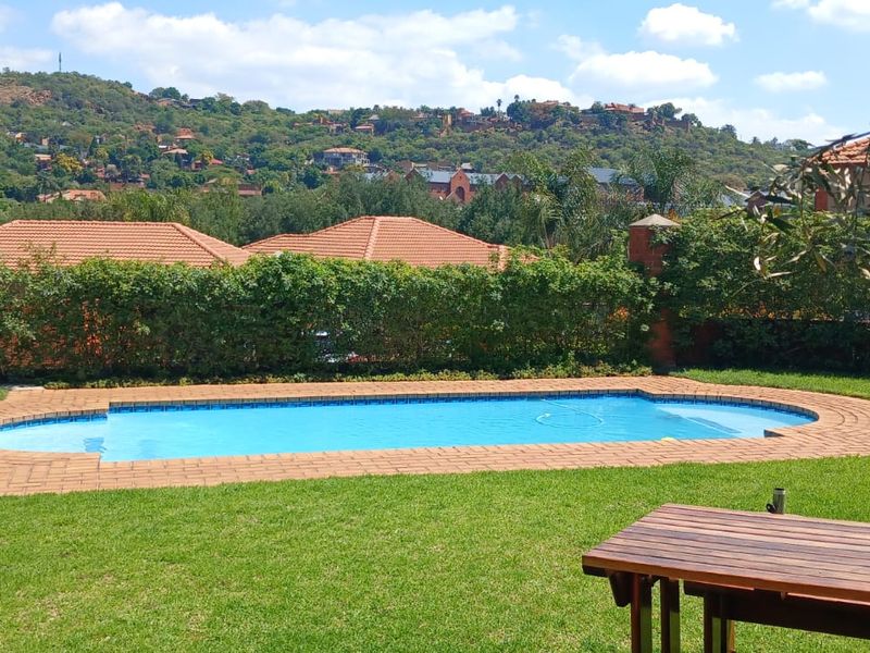 A well-maintained swimming pool set within a landscaped garden, featuring brick coping and scenic hillside views in the background.