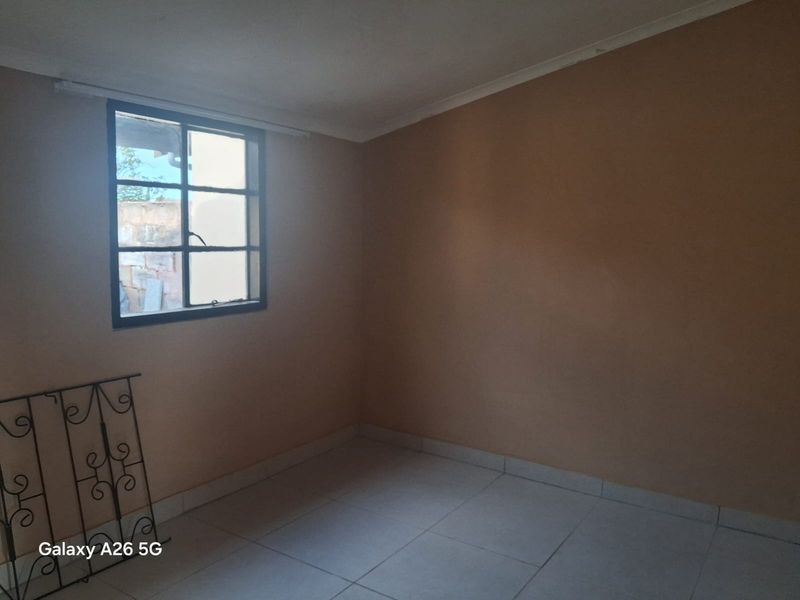 An empty bedroom featuring tiled flooring, a steel-framed window, and coved ceilings, offering a blank canvas for renovation.