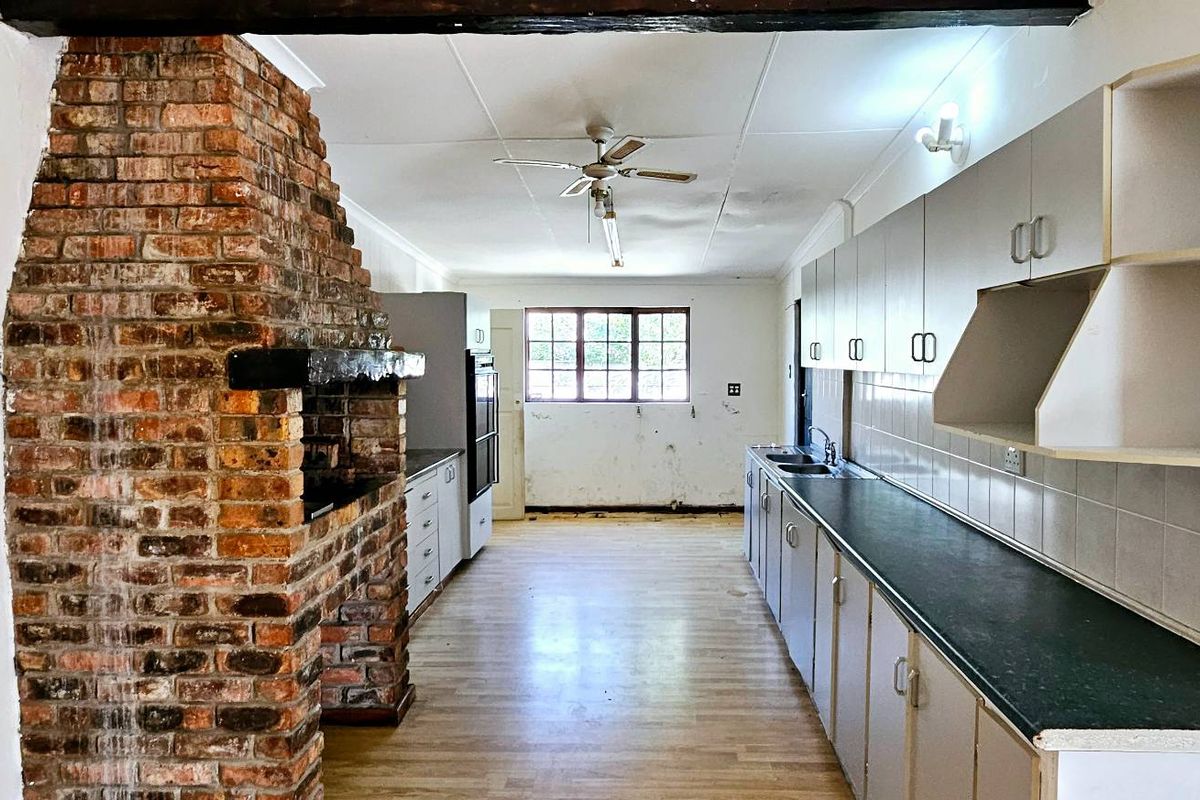 Spacious kitchen featuring a prominent brick fireplace, extensive cabinetry, and laminate flooring, offering significant potential for modernization and renovation.