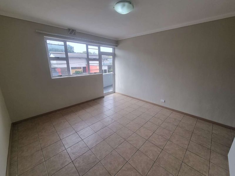 A bright, empty living room featuring neutral walls, tiled flooring, and a large window providing natural light and access to an outdoor area.