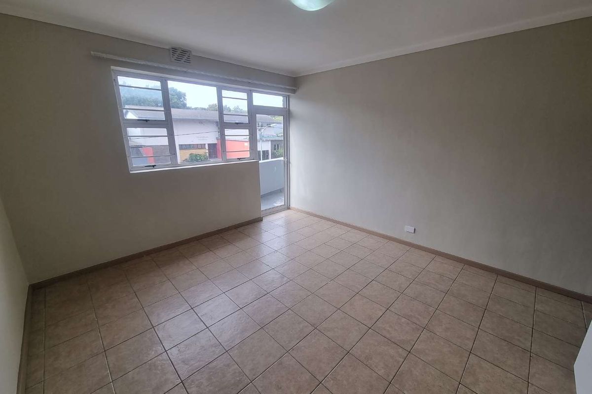 A bright, empty living room featuring neutral walls, tiled flooring, and a large window providing natural light and access to an outdoor area.