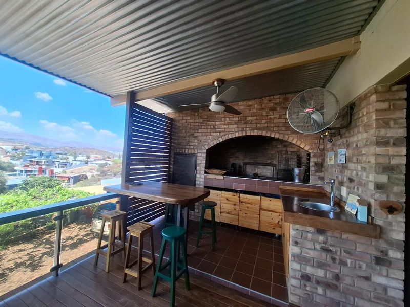 Covered outdoor patio featuring a built-in braai, prep area with sink, and scenic views, perfect for entertaining.