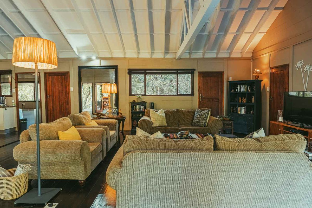 Spacious living room featuring high vaulted ceilings with exposed beams, dark timber flooring, and multiple wooden doors leading to adjacent areas.