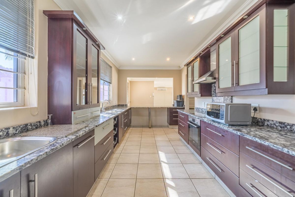 A well-maintained galley-style kitchen featuring dark wood cabinetry, granite countertops, integrated oven, and tiled flooring with ample natural light.