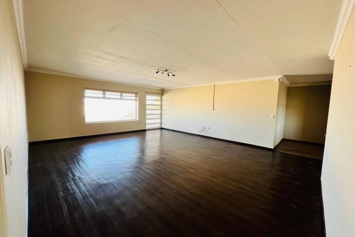 A spacious, empty living room featuring dark wood-look flooring, neutral walls, and a large window providing natural light.