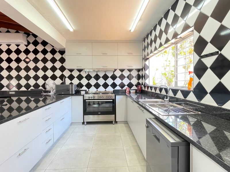 A functional kitchen featuring granite countertops, white cabinetry, a gas stove with oven, and a distinctive black and white diamond-patterned tiled backsplash.