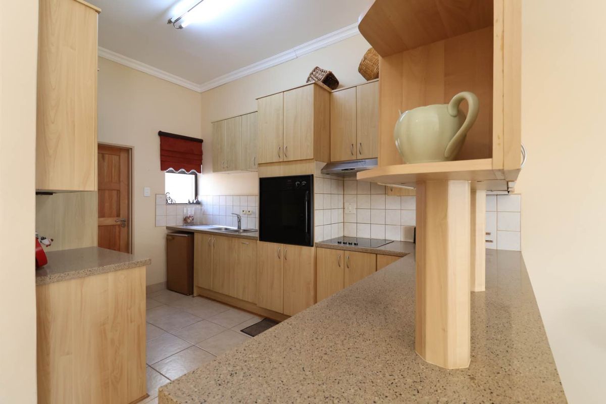 A functional kitchen featuring light wood cabinetry, stone-look countertops, a built-in oven, hob, extractor fan, and tiled flooring.