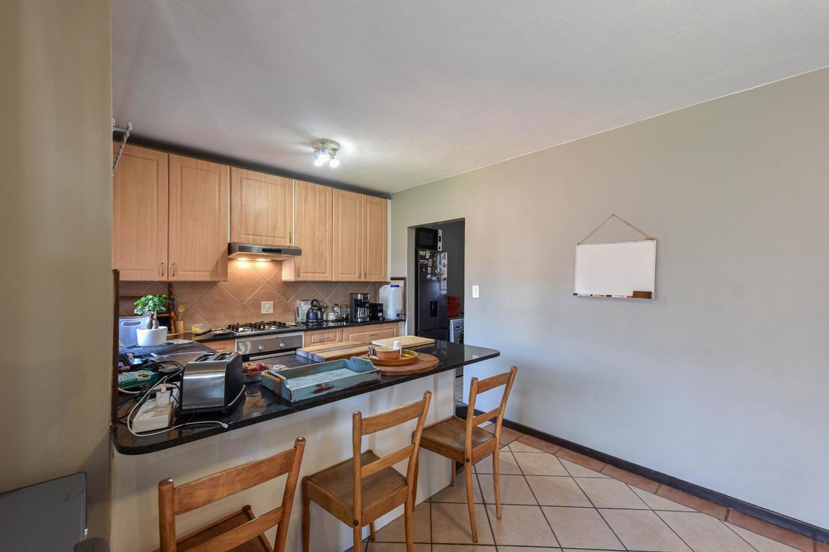 Functional kitchen featuring light wood cabinetry, granite countertops, a breakfast bar, and tiled flooring, with an adjacent scullery area.