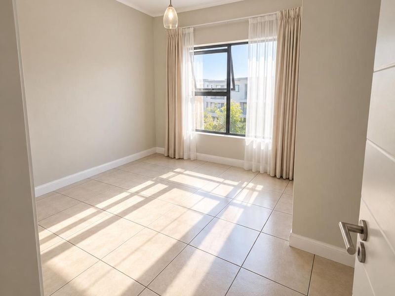 A bright, empty bedroom featuring neutral tiled flooring, a modern pendant light, and large windows allowing for ample natural light.
