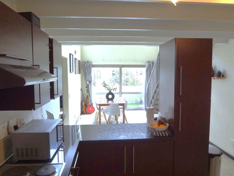 Open plan kitchen and dining area featuring modern cabinetry, stone countertops, and a staircase leading to an upper level with access to a balcony.