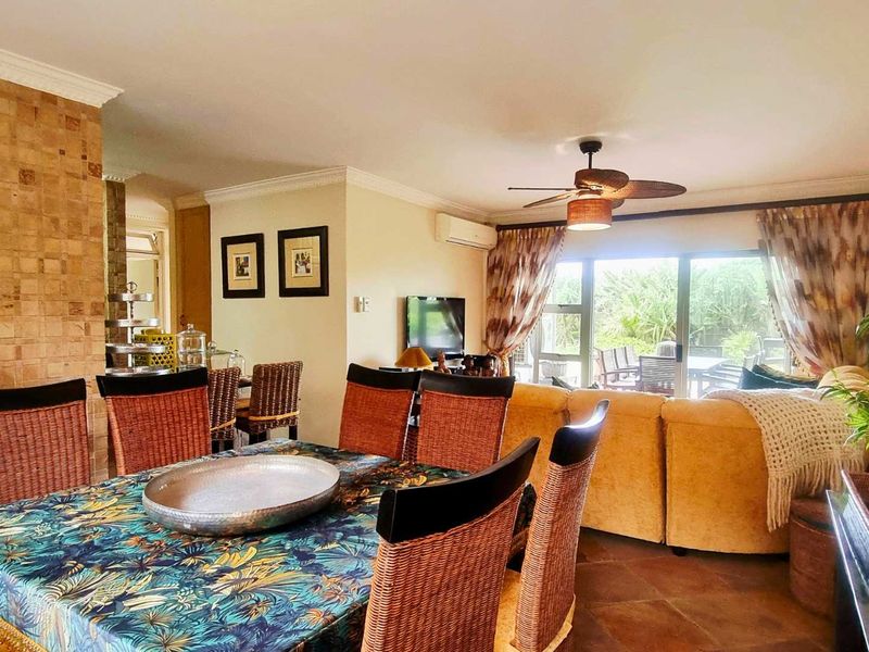 Open-plan living and dining area featuring tiled floors, a stone-clad feature pillar, ceiling fan, air conditioning, and large sliding doors leading to the patio.