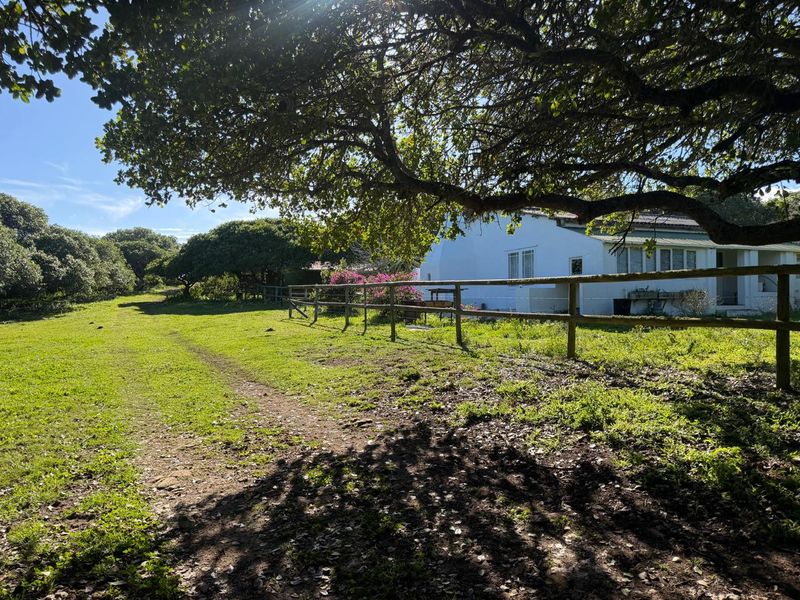 A view of the rear garden area featuring a timber post and rail fence, mature trees, and a white-walled farm building.