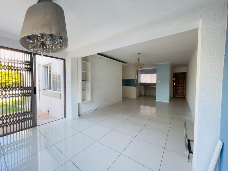 Spacious open-plan living and kitchen area featuring polished porcelain tiles, built-in shelving, and direct access to an outdoor patio through a security gate.