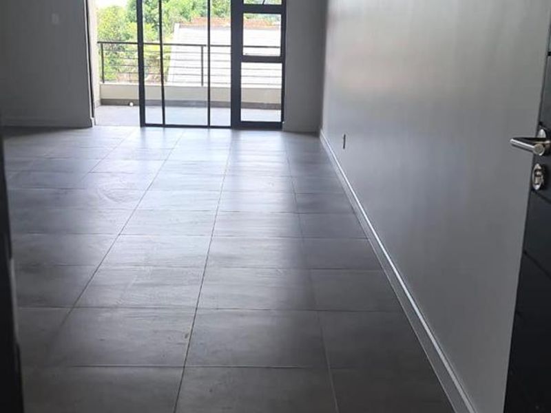 A spacious, empty living area featuring modern grey floor tiles, recessed lighting, and a large sliding glass door leading to an outdoor balcony.