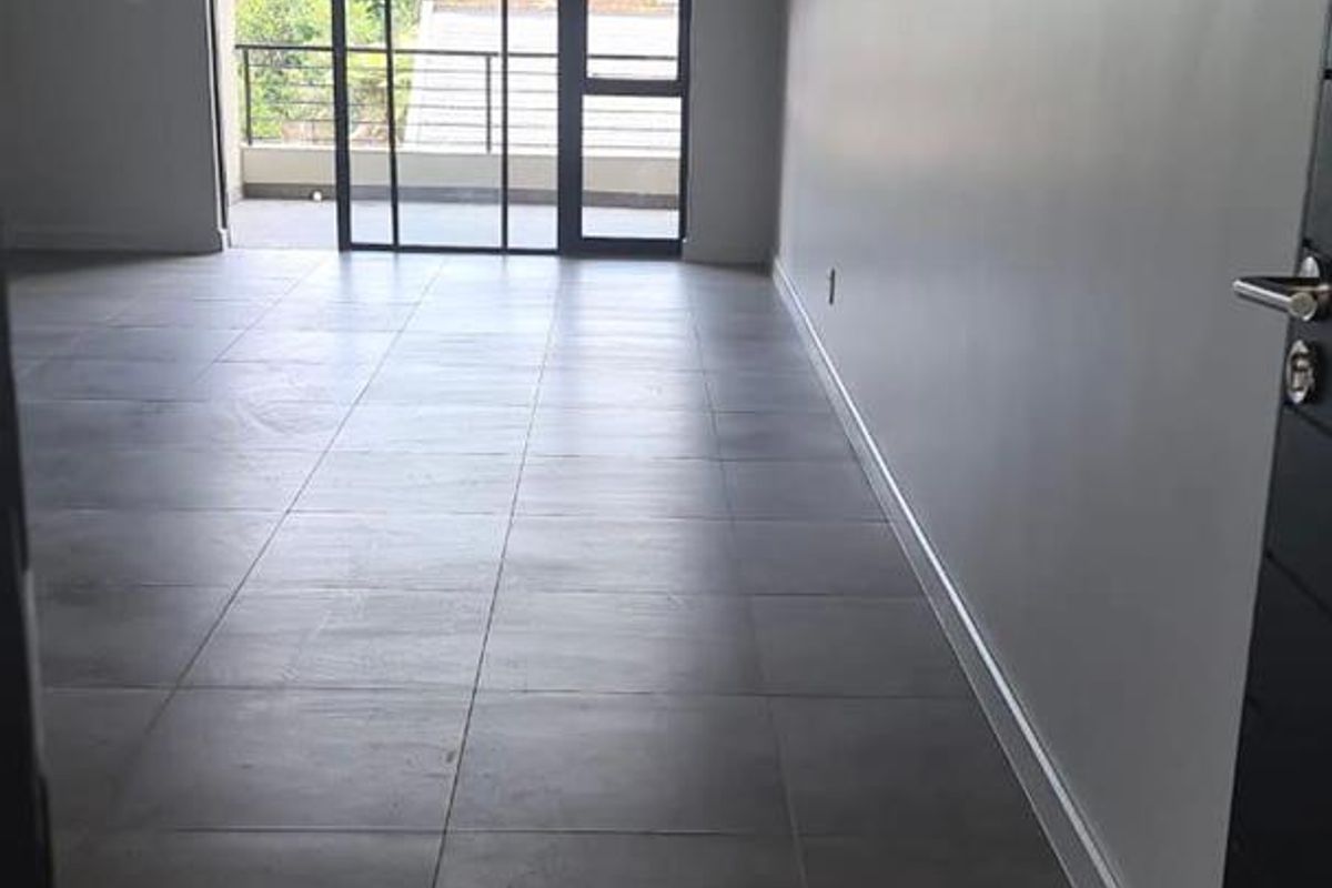 A spacious, empty living area featuring modern grey floor tiles, recessed lighting, and a large sliding glass door leading to an outdoor balcony.