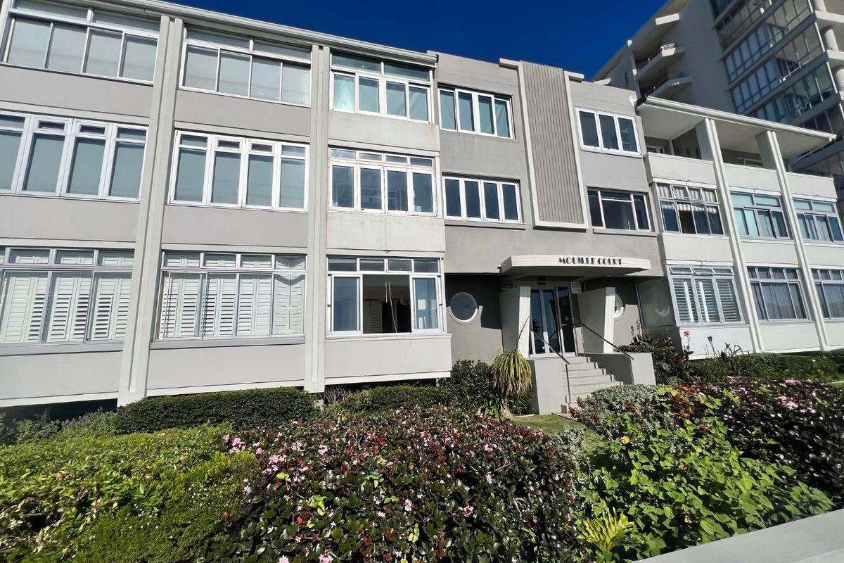 Front elevation of Mouille Court apartment building featuring a multi-story facade with aluminum windows and landscaped garden beds at the entrance.