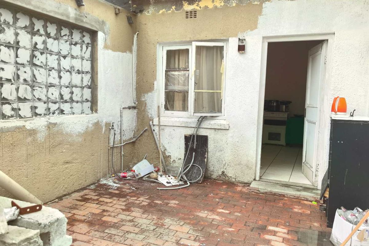 Rear exterior courtyard area featuring brick paving, glass block window, and access to the interior, requiring significant maintenance and cosmetic repair.
