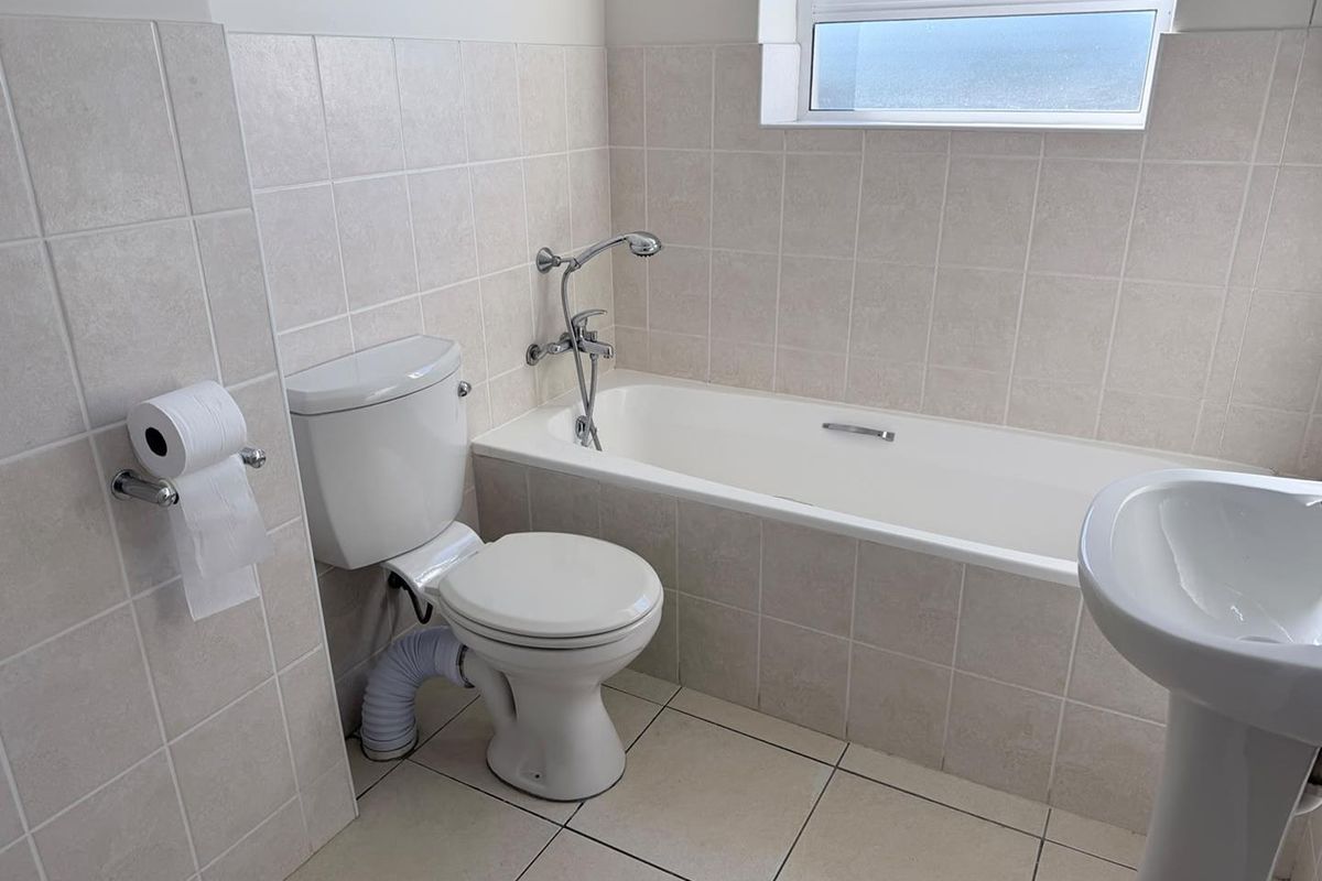 A functional bathroom featuring a bathtub, pedestal basin, and toilet with neutral wall and floor tiling.