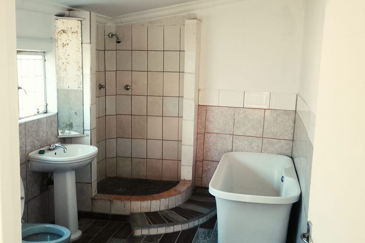 A dated bathroom featuring a pedestal basin, a tiled shower enclosure, and a standalone bathtub with tiled flooring.