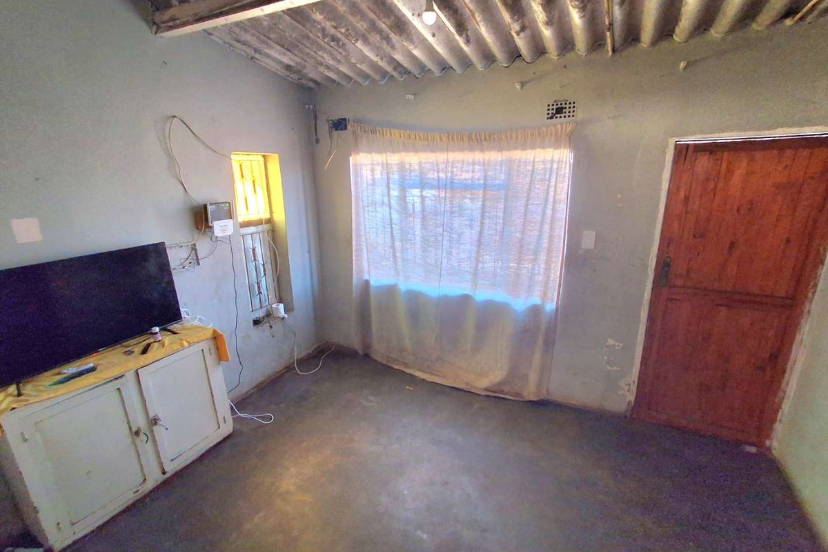 A basic living area featuring exposed corrugated roof sheeting, a timber door, and steel window frames, requiring significant cosmetic updates and finishing.