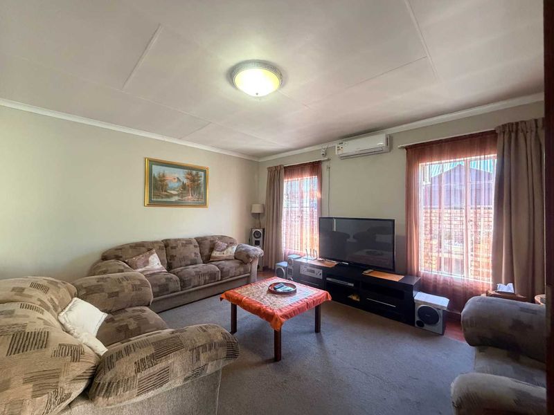 A comfortable living room featuring carpet flooring, a wall-mounted split-system air conditioner, and natural light through dual windows.