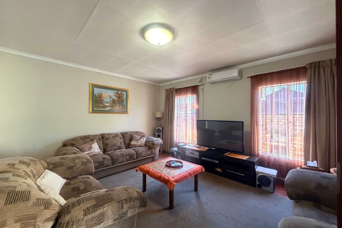 A comfortable living room featuring carpet flooring, a wall-mounted split-system air conditioner, and natural light through dual windows.