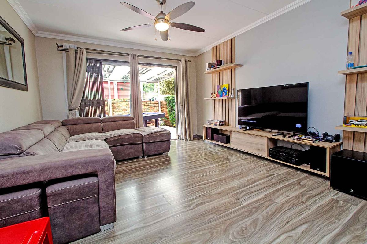 A comfortable living room featuring wood-look laminate flooring, a ceiling fan, and sliding glass doors that open to an outdoor patio area.