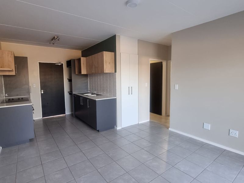 An open-plan living and kitchen area featuring modern grey and wood-tone cabinetry, tiled flooring, and built-in storage cupboards.
