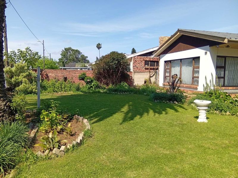 A spacious rear garden featuring a well-maintained lawn, established garden beds, and a brick boundary wall, adjacent to the rear elevation of the house.