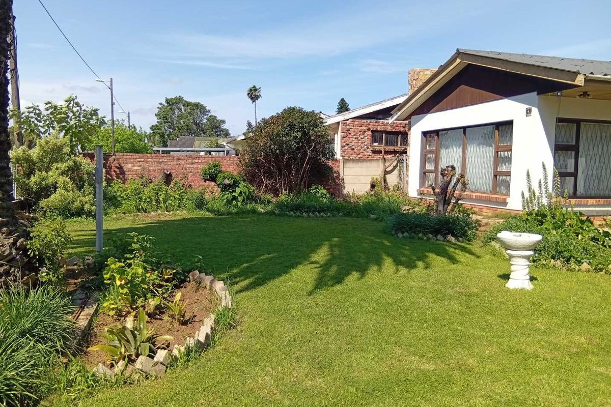 A spacious rear garden featuring a well-maintained lawn, established garden beds, and a brick boundary wall, adjacent to the rear elevation of the house.