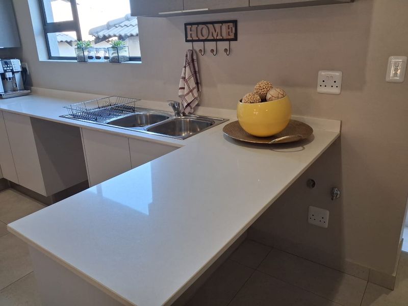 Modern kitchen area featuring clean quartz countertops, double basin sink, and ample built-in cabinetry with neutral tiled flooring.