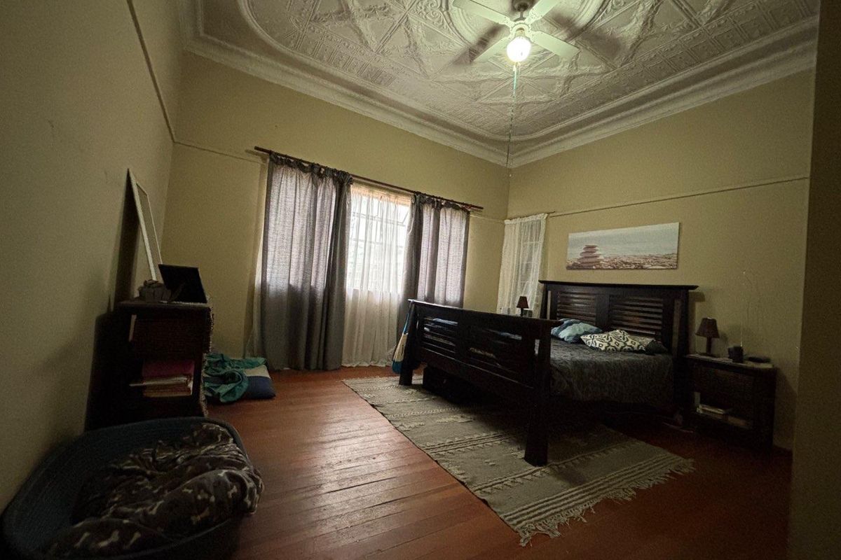 Spacious bedroom featuring original ornate pressed metal ceilings, a ceiling fan, and classic timber floorboards, offering a character-filled living space.