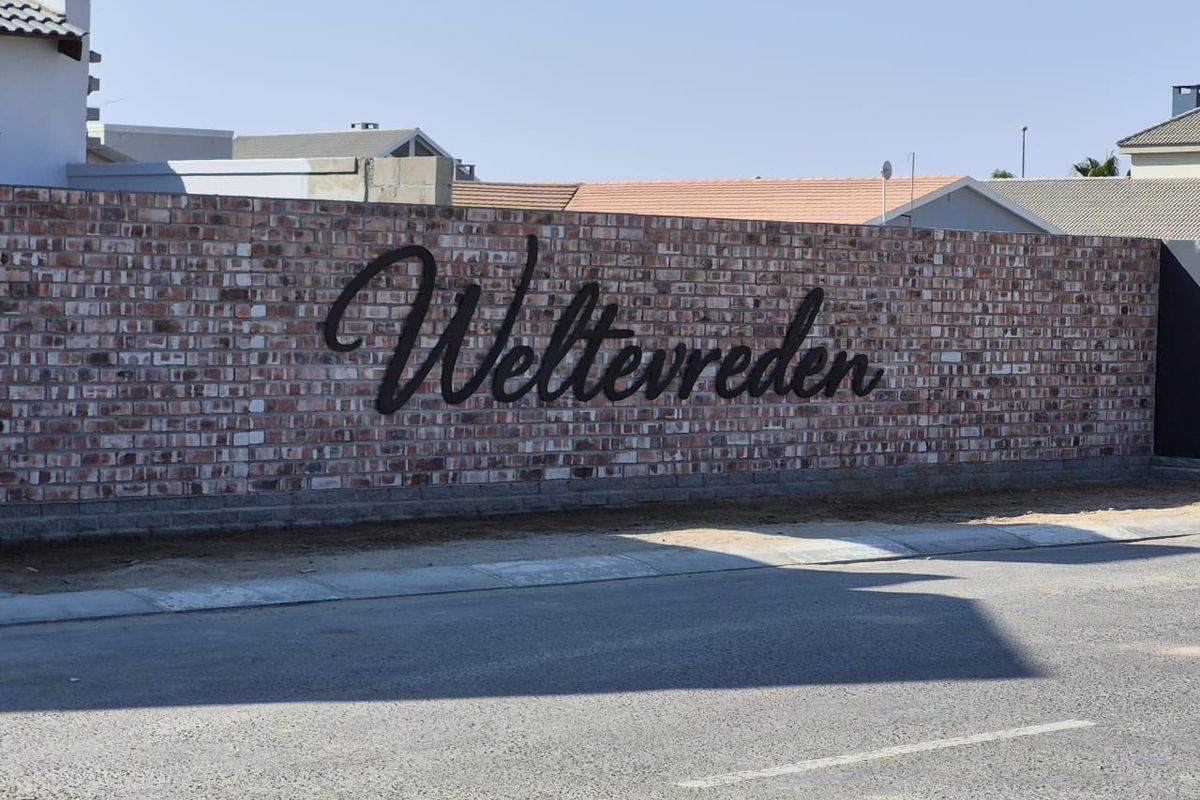 Street view of the Weltevreden estate entrance featuring a prominent brick boundary wall with custom metal signage.