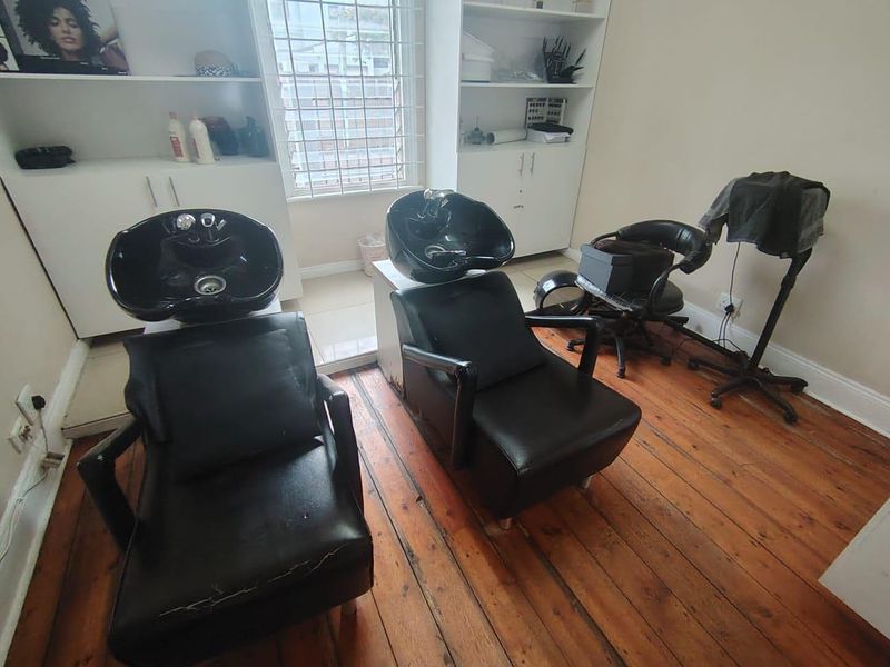 An office space currently utilized as a salon, featuring built-in storage cabinetry, security window bars, and original timber flooring.