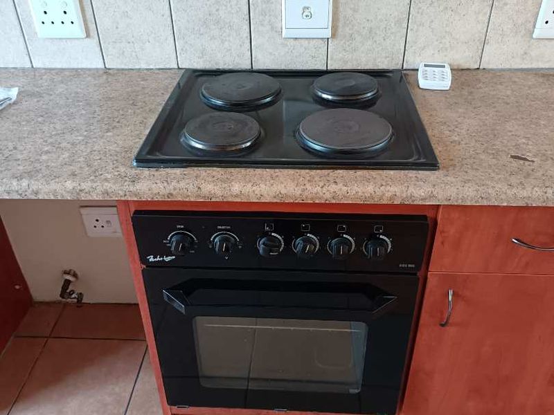 A functional kitchen area featuring a built-in oven, electric hob, tiled backsplash, and wooden cabinetry with ceramic floor tiles.