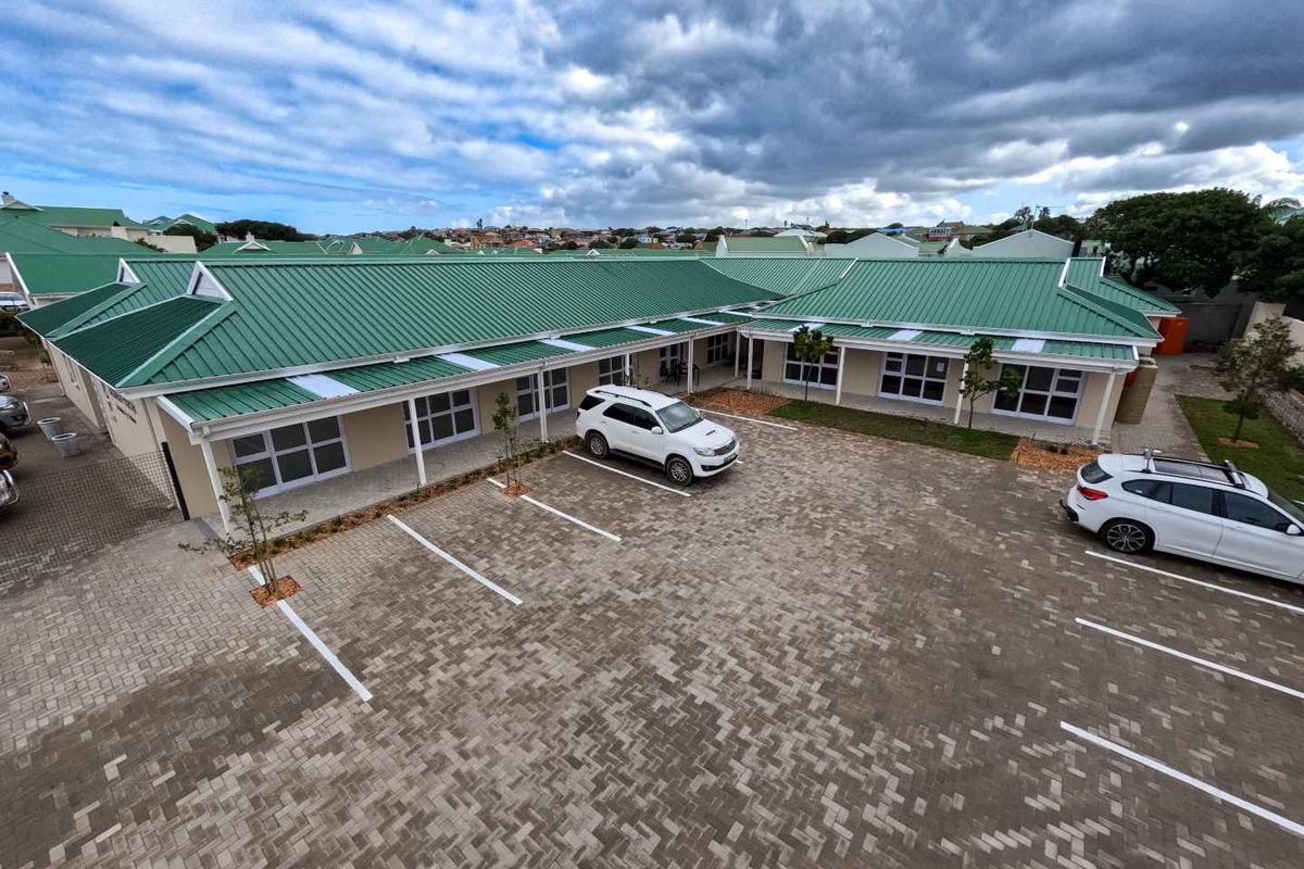 Aerial view of a retirement village complex featuring paved parking areas, green metal roofing, and covered walkways connecting the residential units.