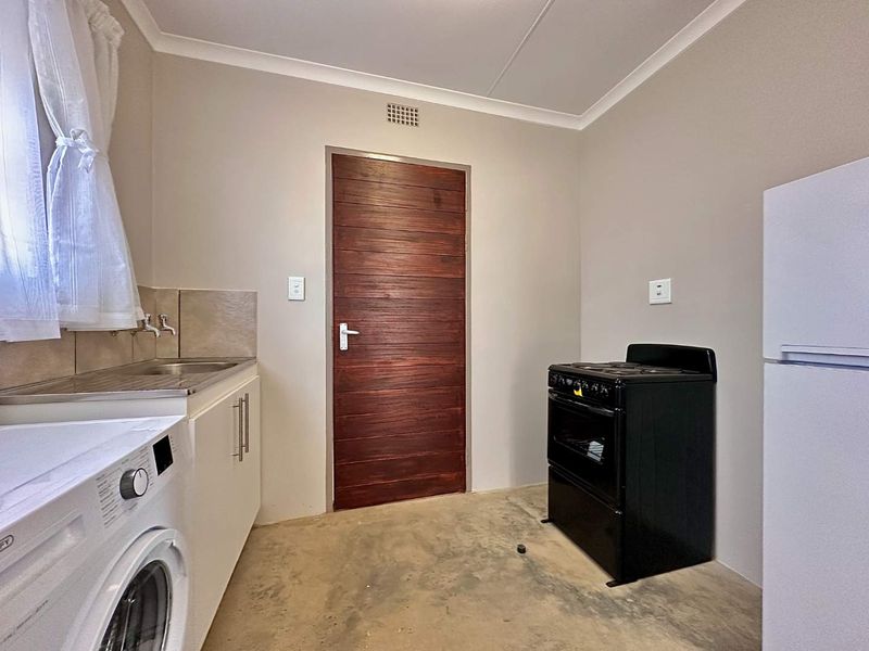 A functional kitchen area featuring a stainless steel sink, tiled splashback, built-in cabinetry, and a ventilation grille, with concrete flooring.