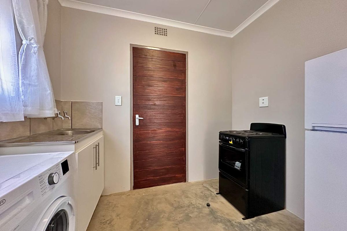 A functional kitchen area featuring a stainless steel sink, tiled splashback, built-in cabinetry, and a ventilation grille, with concrete flooring.