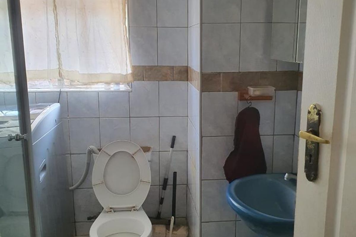 A compact bathroom featuring a pedestal basin, toilet, and integrated laundry space with tiled walls and flooring.