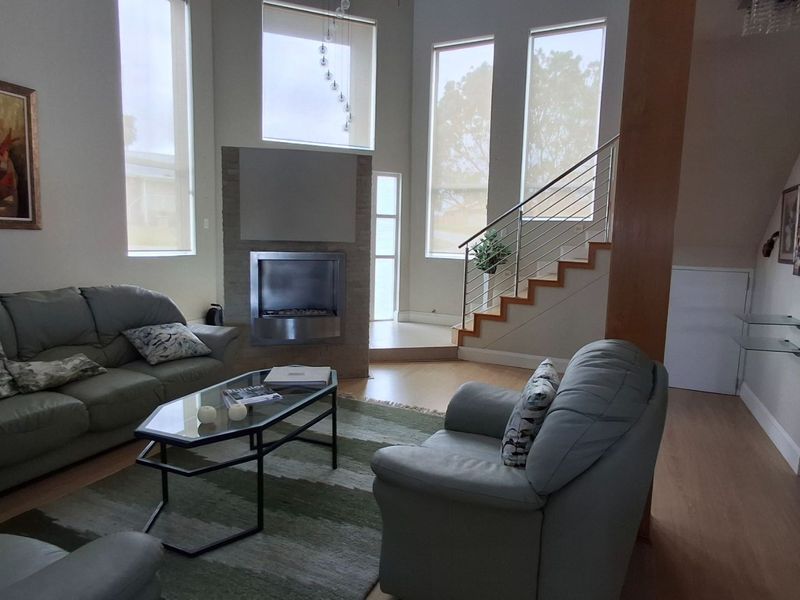 Spacious living room featuring a modern built-in fireplace, high ceilings with large windows, and a contemporary staircase with a stainless steel balustrade.