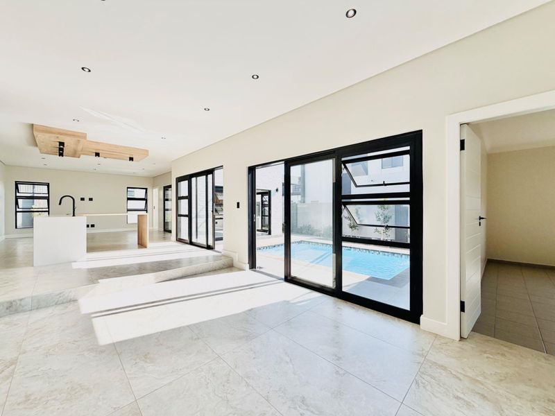 Spacious open-plan living and kitchen area featuring modern finishes, large format floor tiles, and seamless access to an outdoor swimming pool.