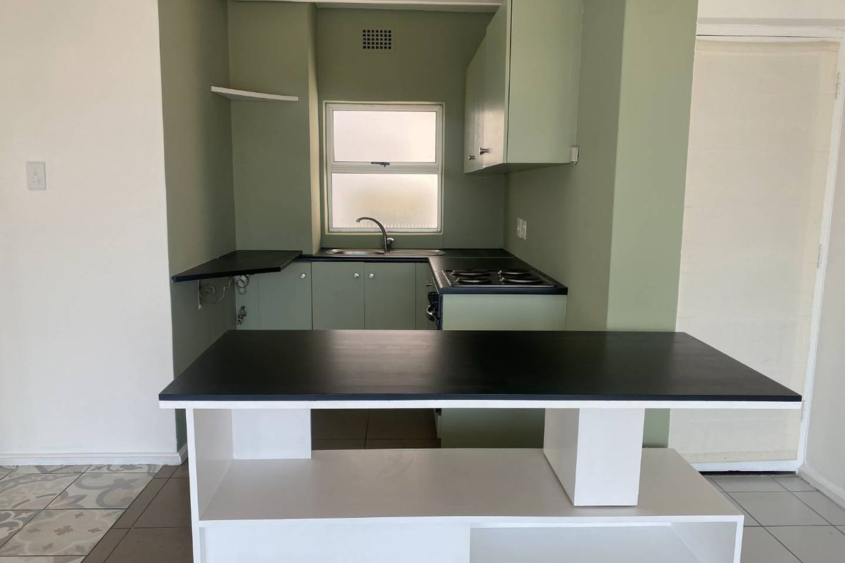 A compact kitchen featuring sage green cabinetry, black countertops, a built-in electric hob, and a stainless steel sink, offering a functional layout.
