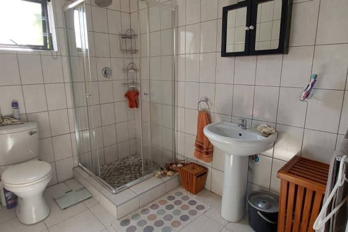 A functional bathroom featuring a corner shower enclosure, pedestal basin, and toilet with full-height wall tiling.