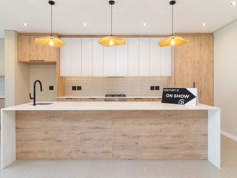 Modern kitchen featuring a large island with stone countertops, sleek wood-grain and white cabinetry, integrated hob, and contemporary pendant lighting.