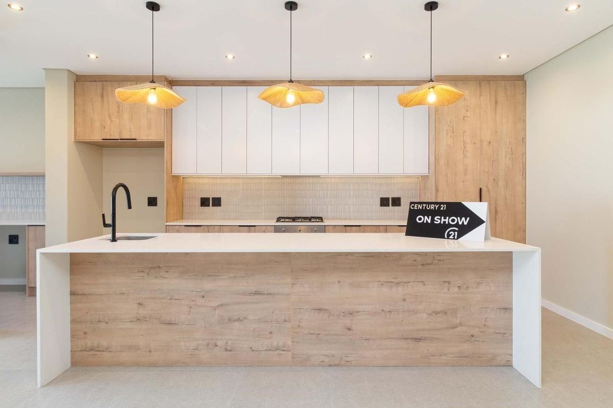 Modern kitchen featuring a large island with stone countertops, sleek wood-grain and white cabinetry, integrated hob, and contemporary pendant lighting.