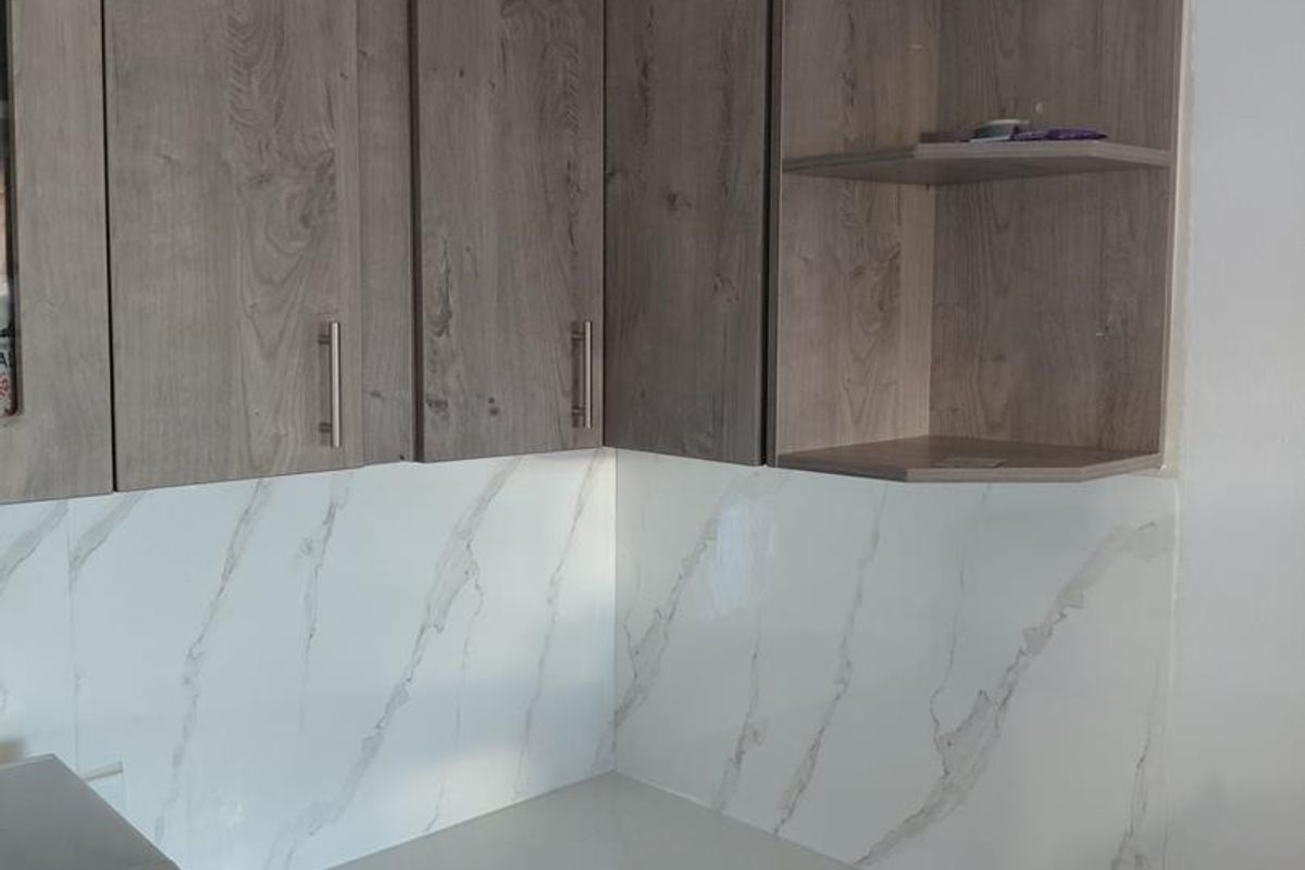 A modern kitchen corner featuring wood-grain laminate cabinetry, a marble-effect splashback, and clean stone-look countertops with an integrated microwave.