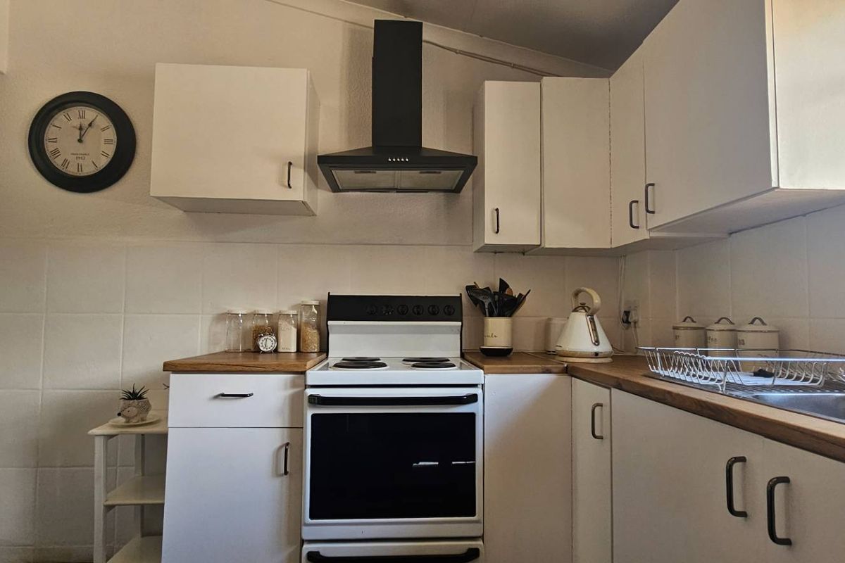 A functional kitchen featuring white cabinetry, wooden countertops, a built-in oven with extractor fan, and tiled splashbacks.