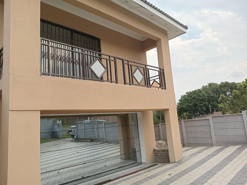 Exterior view of the property featuring a covered balcony with metal balustrades, paved driveway, and secure boundary walling.