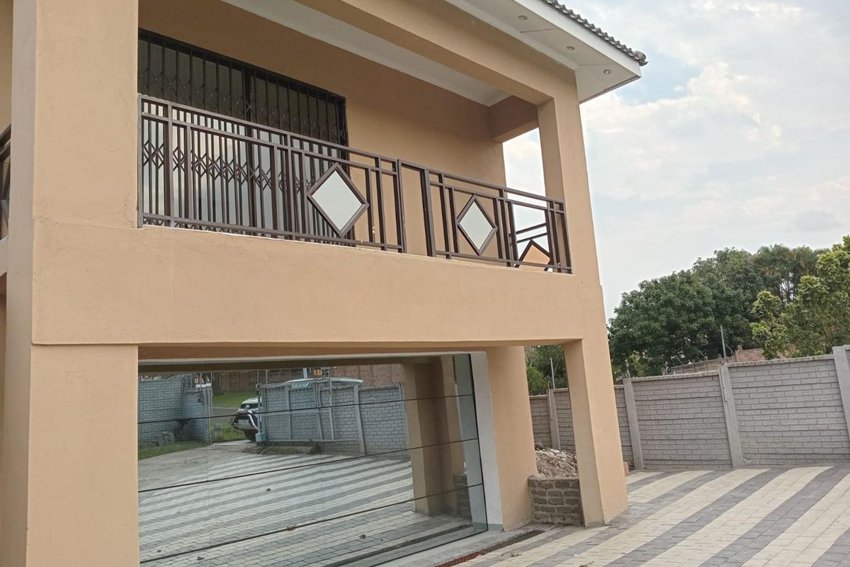 Exterior view of the property featuring a covered balcony with metal balustrades, paved driveway, and secure boundary walling.