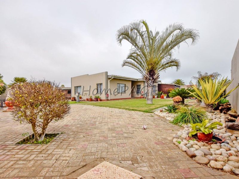 Front view of a single-story house featuring a paved driveway, established garden, and concrete exterior facade.